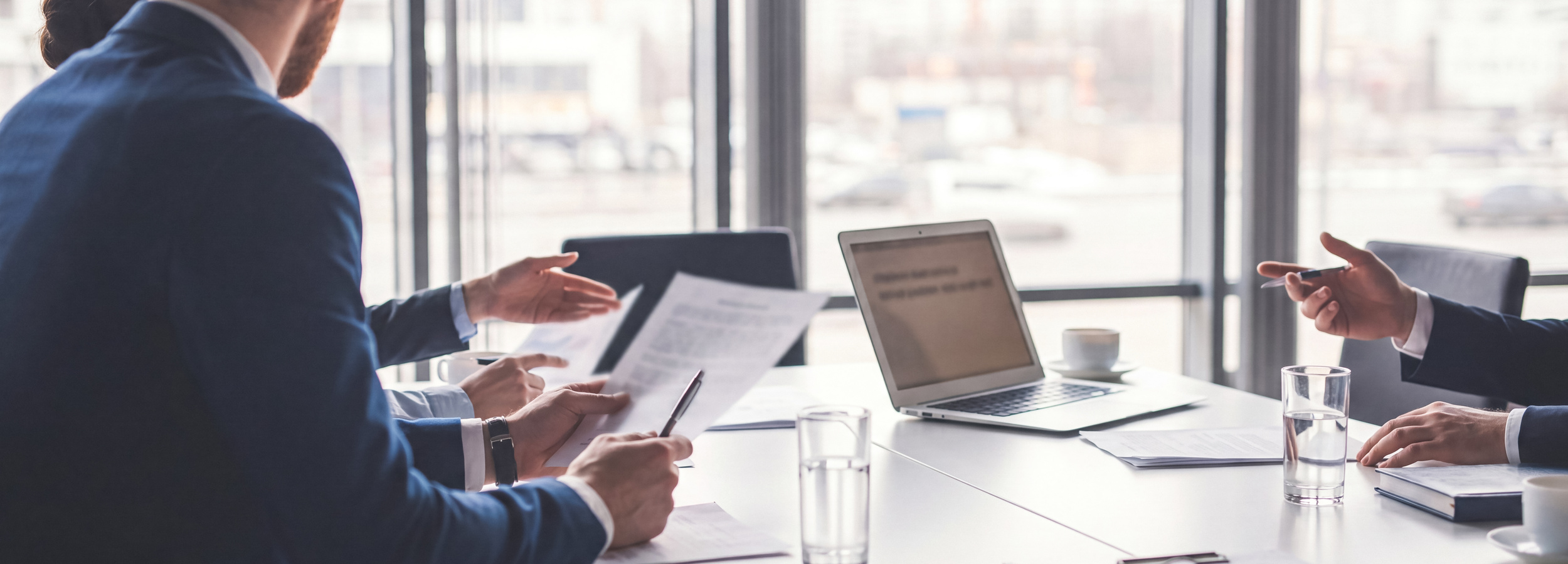 Business people's hands working on documents and laptop at a modern office table with city view.