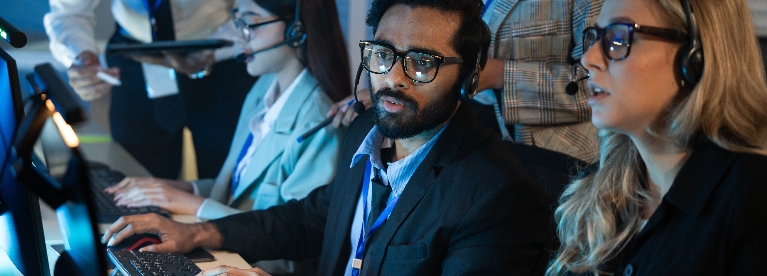 Diverse call center work together late in an office, managing customer support calls with headsets and computers. The team collaborates to solve problems under pressure while handling heavy workloads