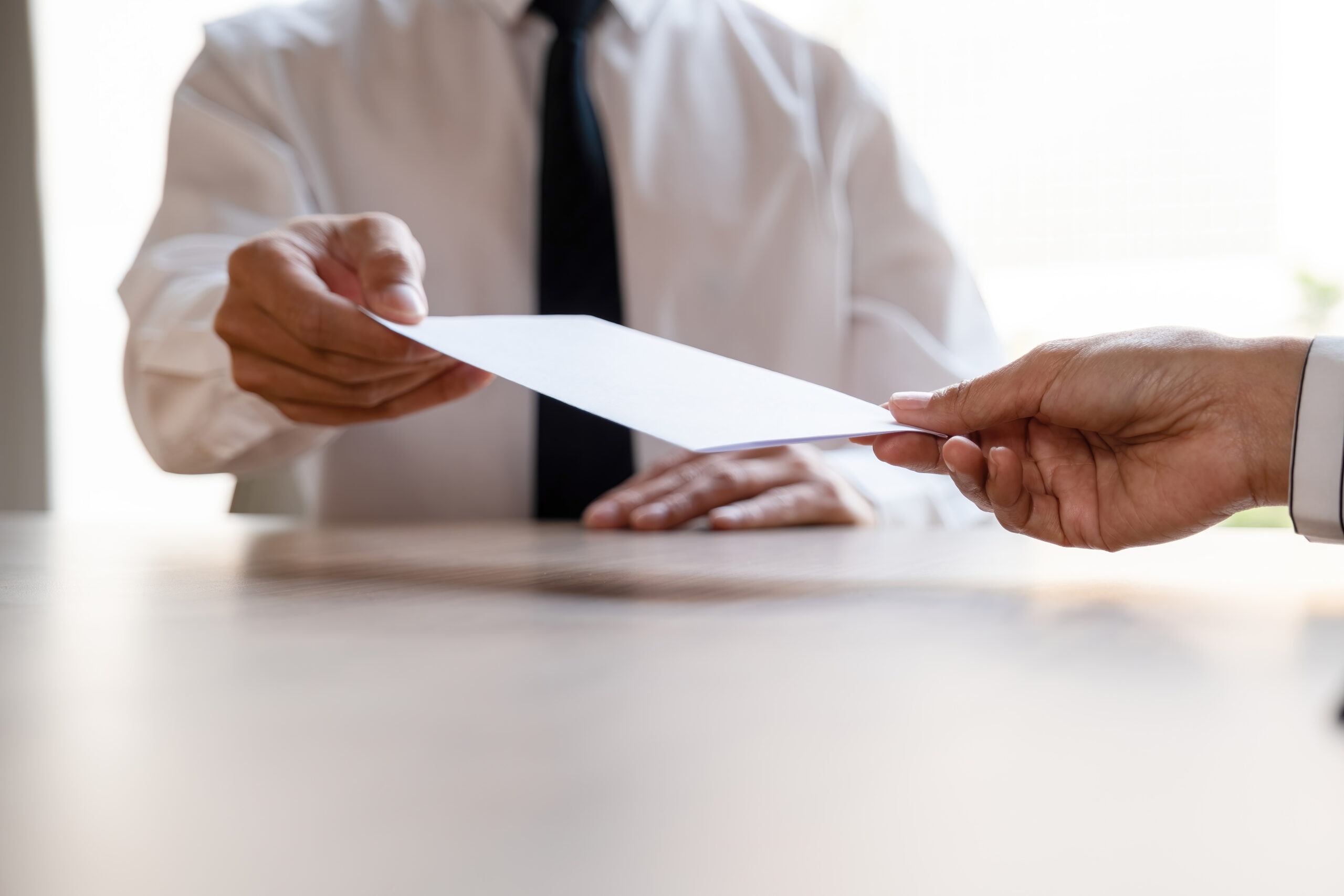 Man giving and handing over his letter of resignation to boss or manager at office desk in workplace, businessman quiting job or being fired from company.